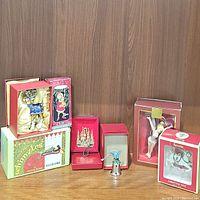 Photo of all 8 assorted hanging Christmas ornaments including the Lenox Tinkerbell in original boxes against wood background.