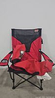 Front view of red and black Coleman folding chair with armrest organizer and cup holders. Chair fabric shows some wrinkles and used condition.