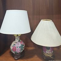 Two lamps on wooden shelf: ceramic floral lamp with white shade and pink tea can lamp with ivory pleated shade.