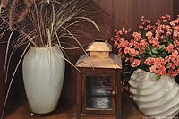 Floral centerpiece with dried grasses in a tall beige ceramic vase, metal decorative lantern on wooden shelf