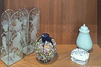 All four decorative pieces arranged on wooden shelf: etched glass candle holders, multicolored vase, light blue lidded jar, blue and white trinket dish.