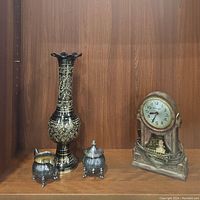 Photo showing the four items: Master Crafters mantel clock, brass vase, silver sugar jar and cream pitcher on a wooden shelf.