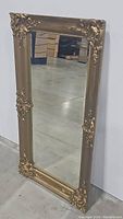 Full view of the rectangular gold framed mirror leaning against a wall, showing size and overall condition.
