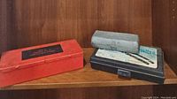 Metal and plastic tool cases on shelf, including red metal box and black plastic case labeled Pop Rivet Gun.