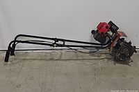 Side view of the Troy-Bilt mini tiller showing the engine, metal tines, and handle length.