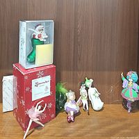 Overall display of assorted Christmas ornaments including boxed Santa in stocking, ballerina, nutcracker box, and various character figurines.