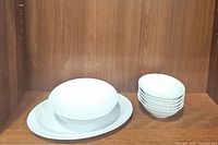 View of scalloped white china oval platter, serving bowl, and stacked cereal bowls on shelf