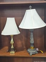 Set of three lamps: one tall etched Stiffel lamp in grayish metal with ornate base and white fabric shade; two smaller brass lamps with rounded bases and rectangular white fabric shades.