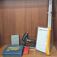 Photo showing Craftsman Automatic Drill Index, tubing tool set in blue metal case, Craftsman electric stapler in black and red, red metal accessory, large white grid measuring tool with orange frame