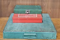 Three metal tool kits stacked with largest blue box on bottom, medium greenish box in middle, small red box on top