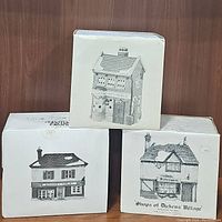 Three boxes of hand painted porcelain village collectible shops showing front illustrations of each building.