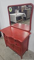 Front view of the red painted wooden dresser with matched framed mirror attached, showing curved drawer fronts and rounded mirror edges.