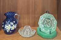 Cobalt blue glass beverage pitcher with white painted flowers, clear handle, cut glass trinket dish, and six green depression glass plates on display