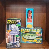 Photo showing Easy Money box, Hula Doll box, Big Mouth Billy Bass box all displayed on wood shelf