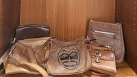 Five assorted brown handbags grouped on shelf showing varying sizes, colors, and styles