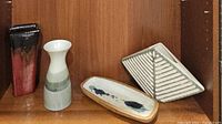 Photo showing four items: red and black glazed tall vase, two-toned Otagiri vase, diamond-shaped textured white vase, and painted rectangular plate.