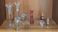 Overview of entire lot showing candlestick holders, silver-rimmed glasses, cranberry vase, compote, and perfume bottles all displayed on wooden shelf
