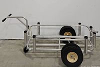 Side view of the metal fishing cart showing aluminum framework, large wheels, and handle with foam grips.