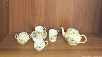 Full set displayed on wooden shelf including teapot, sugar bowl, creamer, two tea cups, and two saucers showing overall set condition and items included.