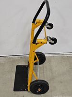 Side view showing yellow metal frame with black expandable handle, base platform, two large wheels and smaller swivel casters.