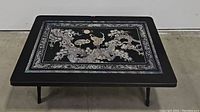 Front view of low profile black foldable table with detailed crane and tree gold and white inlay design.