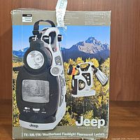 Boxed Jeep branded multifunctional electronics device with TV, AM/FM Weatherband radio, flashlight, and fluorescent lantern capabilities shown on front of box.