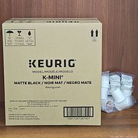 Box of Keurig K-Mini matte black coffee maker with label and bar code, showing brand, model, and manufacturing details.