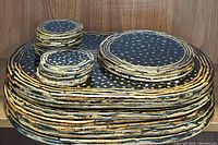 Stack of black lacquer placemats, coasters, and hot plates with gold spots and textured gold edges in black background.