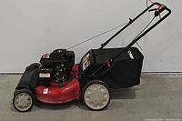 Side view of red Troy-Bilt TB240 lawn mower with black collection bag and white wheels on concrete floor.