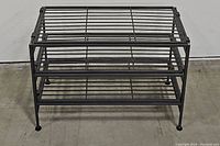 Front view of black 3-tier metal shoe rack showing three shelves made of metal rods and four legs with floor protectors.