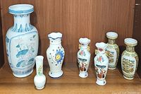 Photo showing seven porcelain vases including tall blue accented vase, yellow floral vase, moon & sun vase, pair of vintage gold trimmed Japanese vases, and other small floral vases.