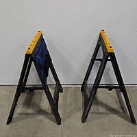 Pair of black folding pocket sawhorses with yellow tops standing open.