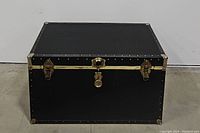 Photo of the vintage black steamer trunk closed, showing metal corner protectors and three front locking clasps.