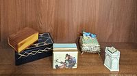 Six vintage trinket boxes arranged on a wood shelf, showing different materials and designs including brass, wood, porcelain, and painted boxes.