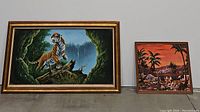 Front view showing both paintings: large tiger painting on left with gold frame, smaller tropical sunset painting on right with dark wood frame