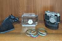 Display of all items including camera, clock, horse bookend, and bracelets on wooden shelf.