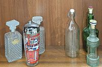 Full view of all six vintage glass bottles and cocktail shaker showing variety of glass types and designs