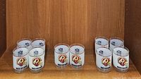 Set of 10 vintage whiskey tumblers displaying Washington Redskins helmet logos and NFL shield logos in frosted glass design on a wooden shelf.