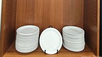 Stacks of white round dinner plates with one plate displayed upright to show the front design and shape.