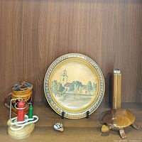 Photo showing wooden container, painted wooden plate with church scene, fishing bobber puzzle, clay whistle, and kaleidoscope on wooden shelf.
