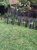 Five black outdoor chairs on grass: four stackable chairs and one king swivel chair.