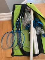 Photo of three badminton rackets, net poles, net, shuttlecocks and carrying bag all placed on wooden floor