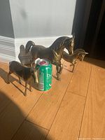 Three brass horse figurines arranged next to a soda can for size reference, showing their relative sizes and details.