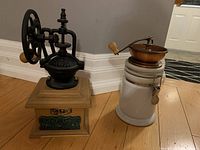 Two vintage coffee grinders side by side on wooden floor against wall.