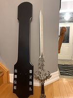 Full view of sword next to black mounting plaque, showing sword size and shape