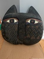 Front view of the black cat head sculpture showing large eyes and geometric cheek patterns