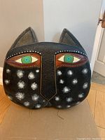 Front view of decorative cat head sculpture showing its textured black finish with white spots and green eyes.