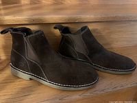 Side view of the pair of dark brown suede Chelsea boots with white stitching, showing shape and sole detail.