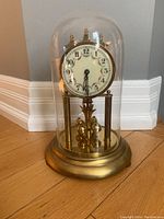 Front view of German made anniversary 400-day clock under clear glass dome on brass base showing dial and pendulum detail.