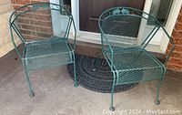 Photo of two green metal patio chairs with mesh seats and backs, and decorative grapevine design.